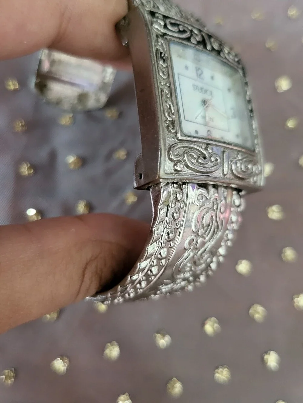 Silver bracelet watch with ornate scrollwork design has antique white face